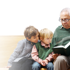 Older man sitting and reading a book to two young boys sat beside him on a wooden bench