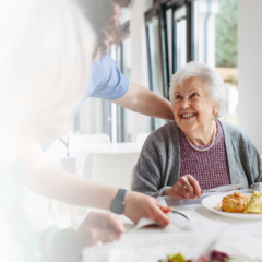 Senior woman enjoying a meal with caregiver support during a respite care stay